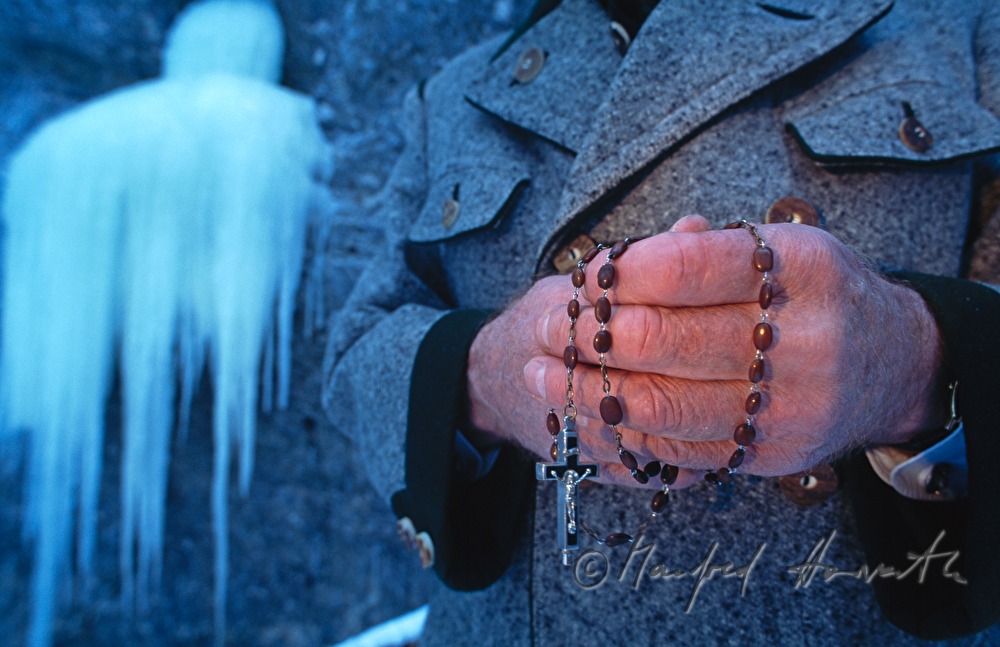 pilgrim with rosary prays near a frozen waterfall