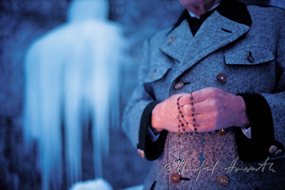 pilgrim with rosary prays near a frozen waterfall
