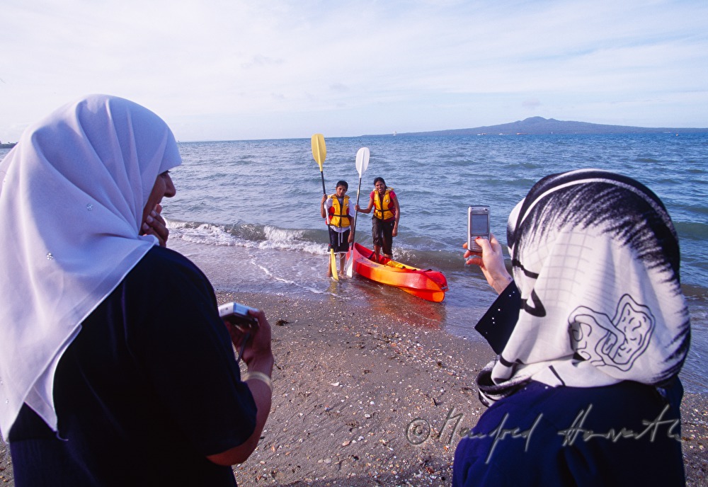 indian tourists on the beach take a photo of two kayakers