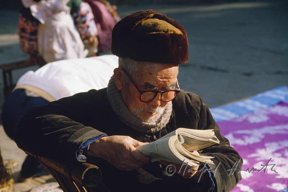 man reading a book in front of his house