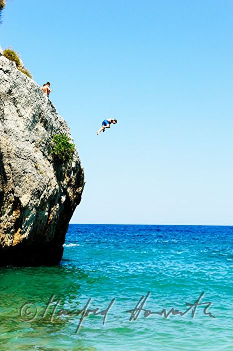 kids jump from a rock into the ocean