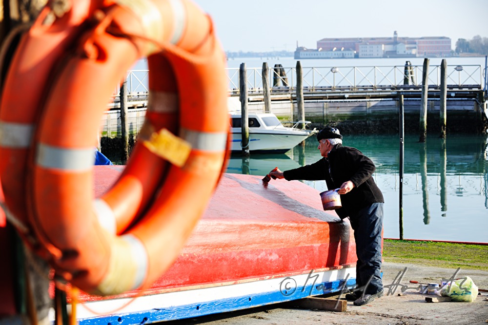 painter works a boats in front of a shipyard
