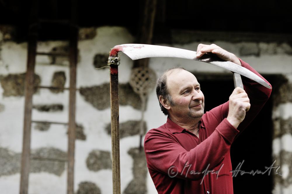 farmer sharpening his skythe with a grindstone